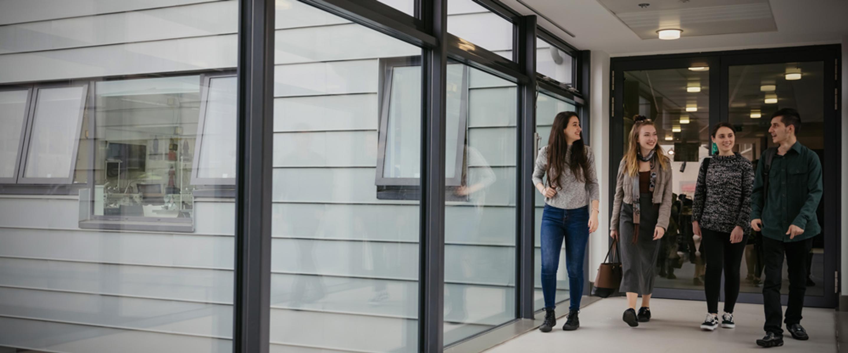 A group of students walk down a glass corridor in a university building