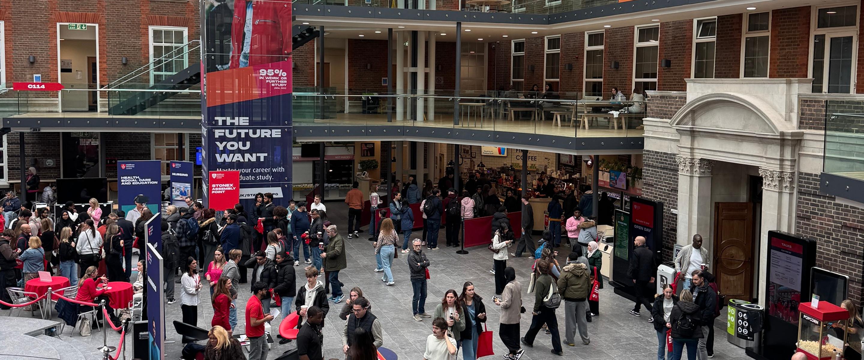 Three smiling students in red t-shirts with a sign that points to open day registration
