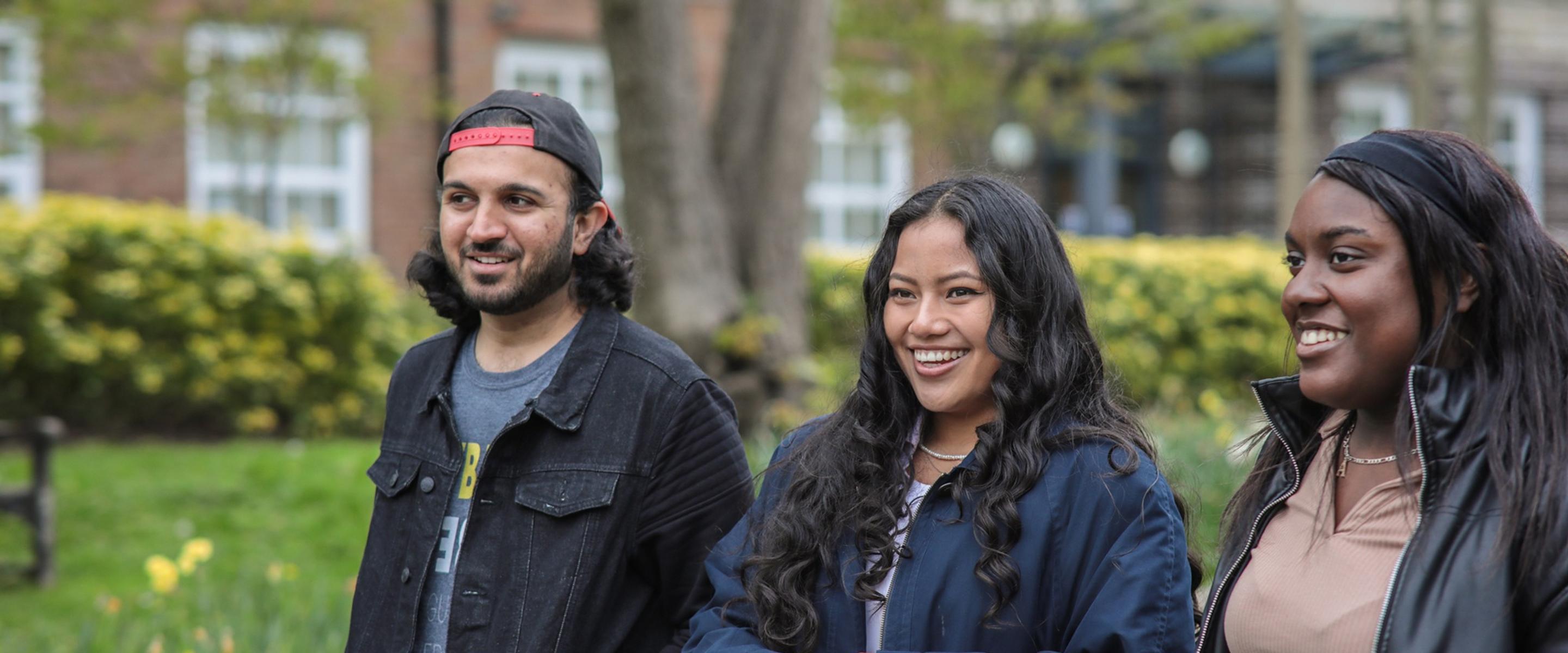 Three smiling students walking alongside each other through Middlesex University London's leafy campus
