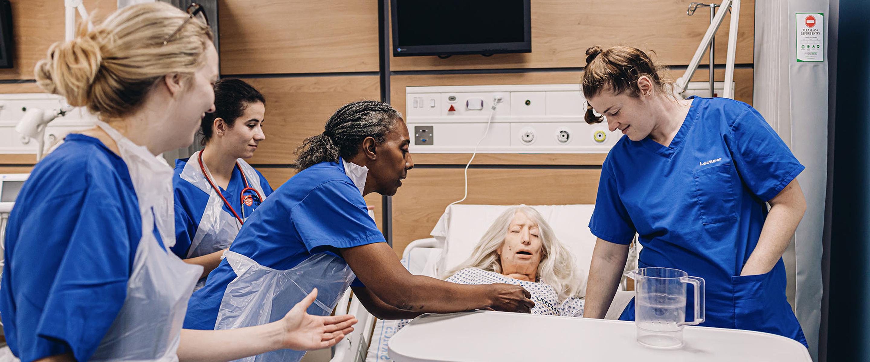 nurse demos procedure with dummy while student nurses watch on