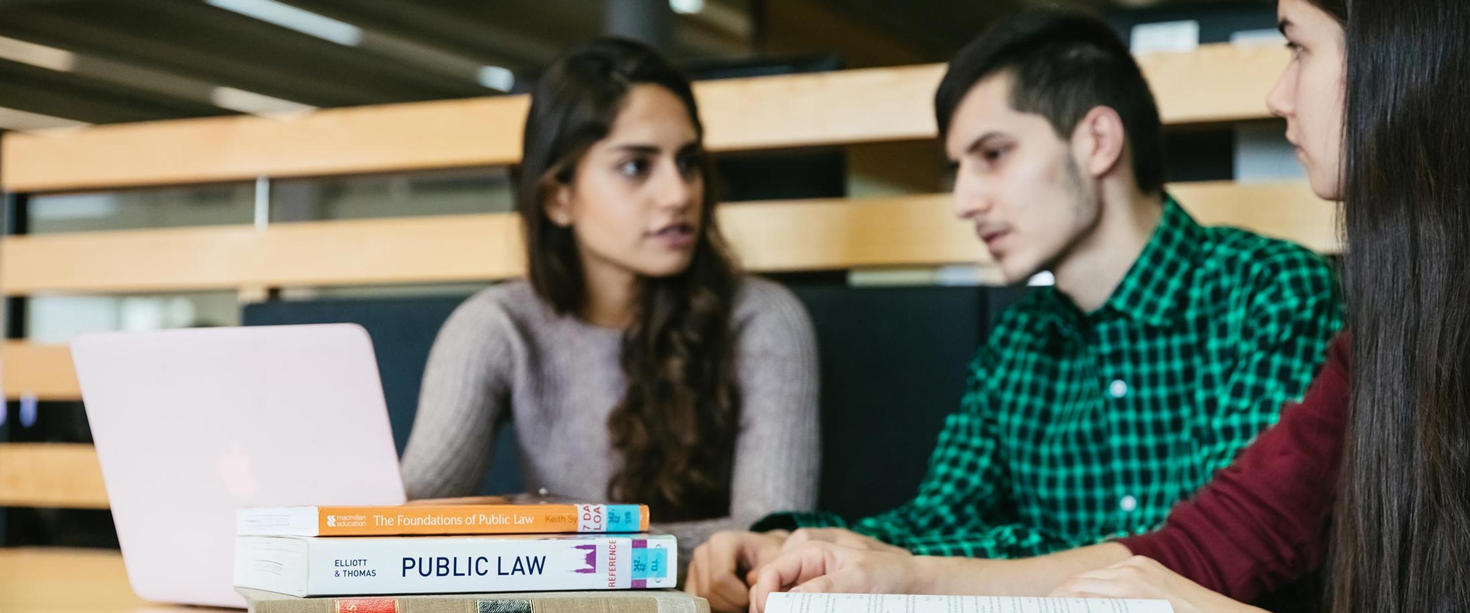 Three law students sat at desk looking at a laptop and books.