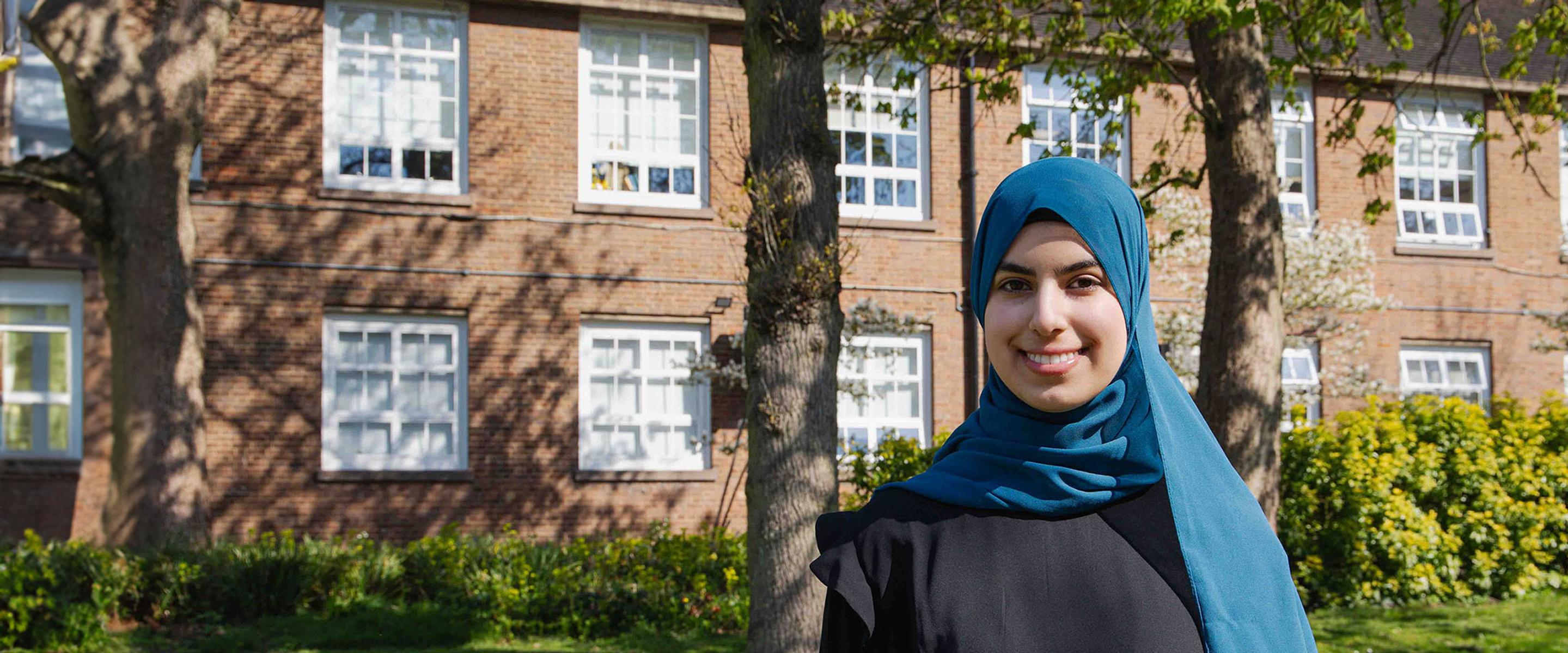 Duha stood on campus on a sunny day with campus building in background