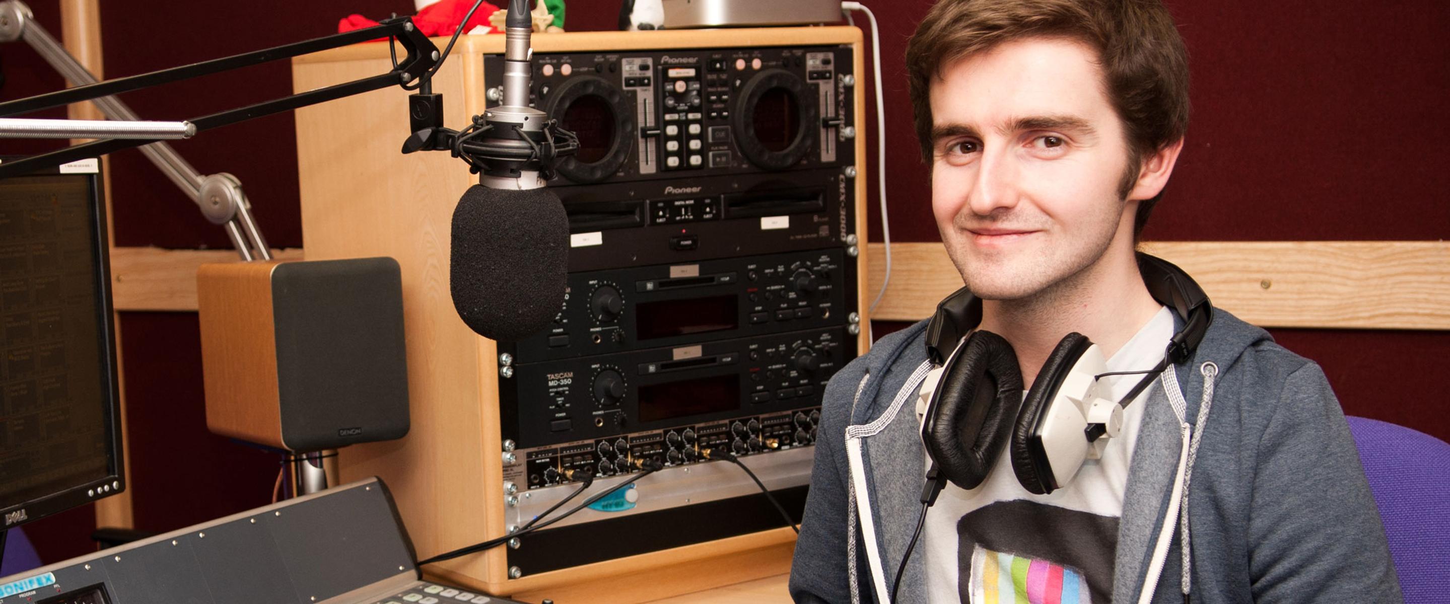Male student wearing headphones sitting in front of a music mixer device