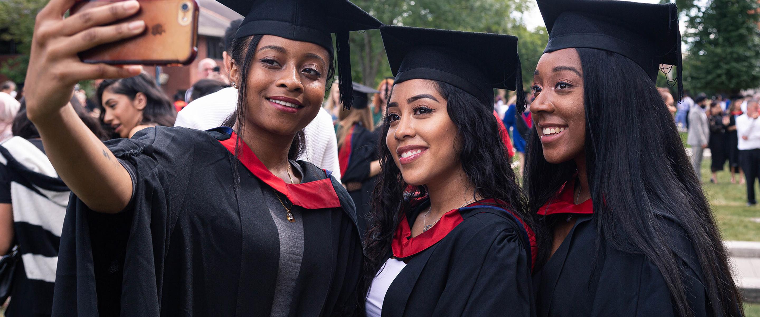 Three female students wearing graduation robes take a selfie