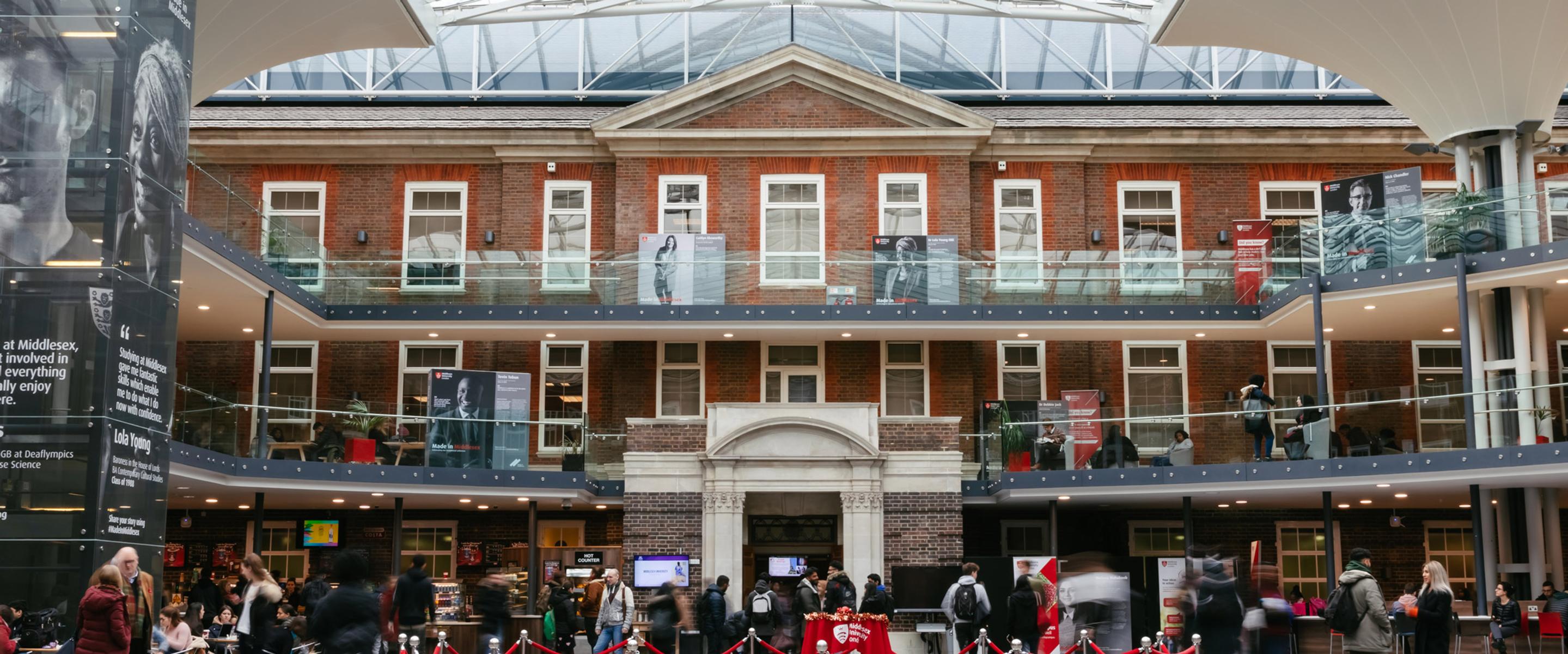 Atrium of a red brick building with glass ceilings and groups of people hanging around.