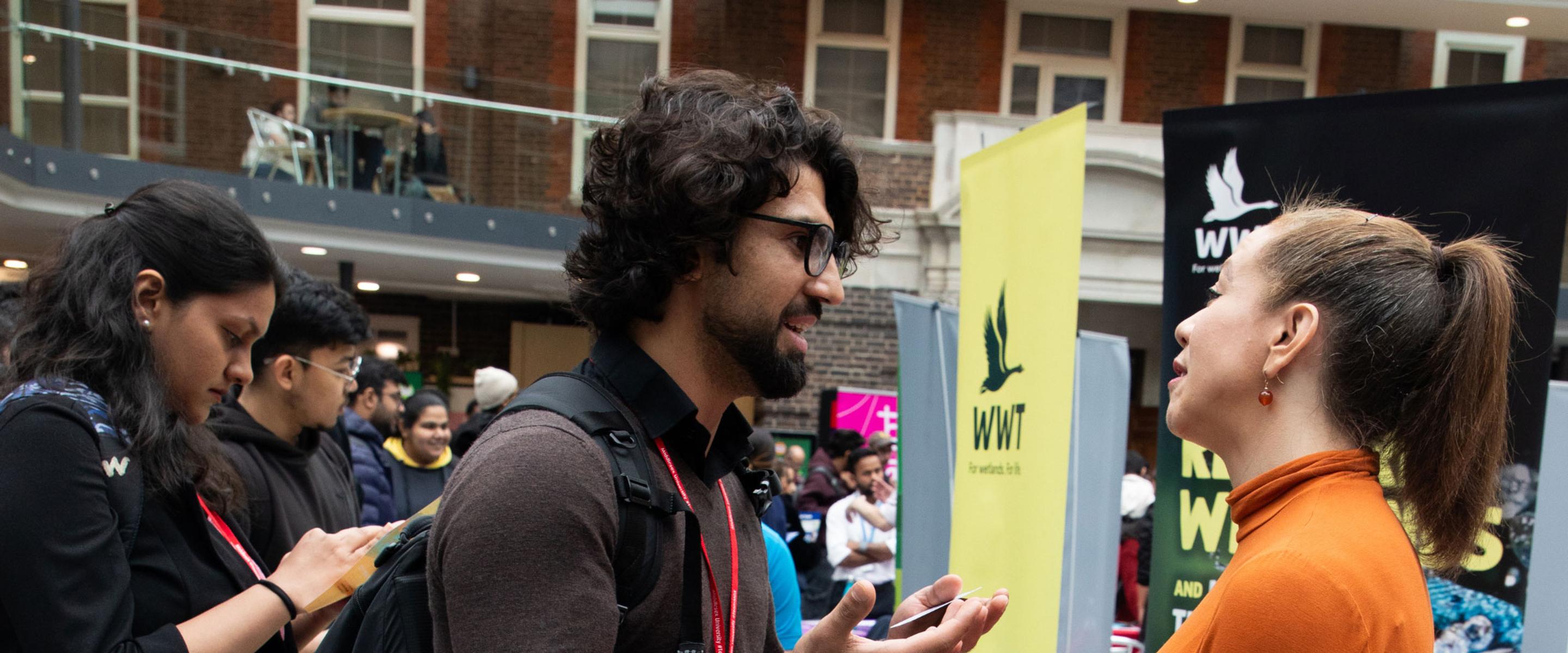 A young man talks to a young woman at an event in a building