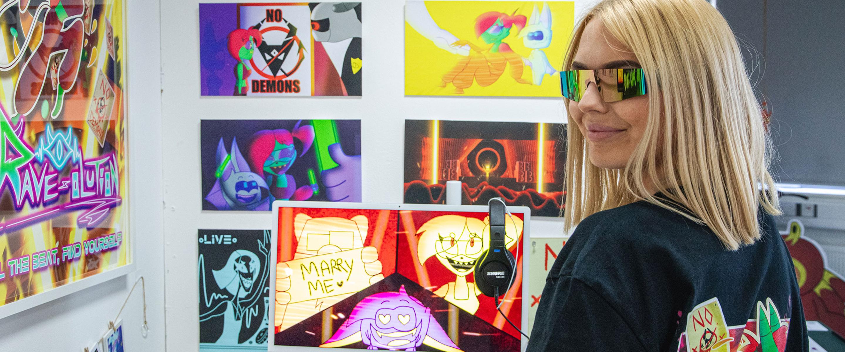 Girl wearing glasses stood in front of gallery of animation work