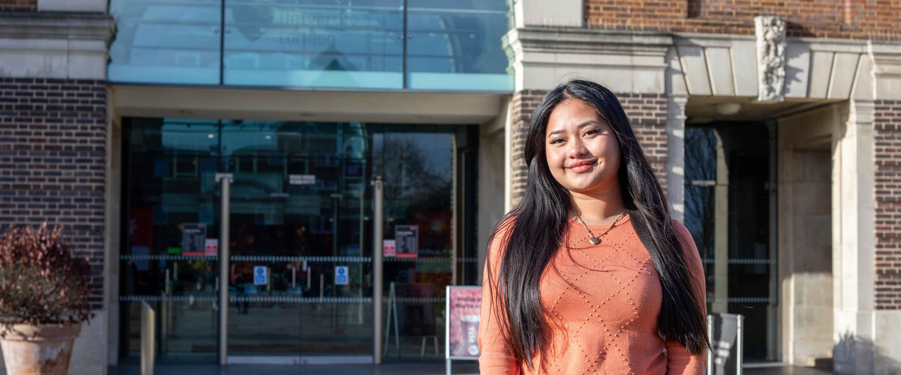 Smiling female student in front of a red brick building reading middlesex university