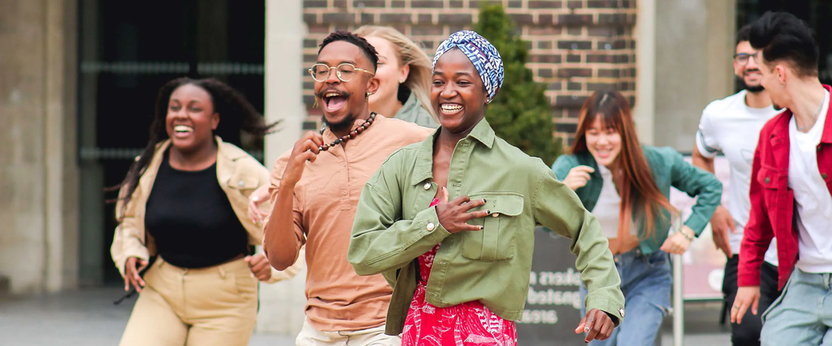 Diverse group of students running together outdoors on campus, smiling and laughing during a university open day activity
