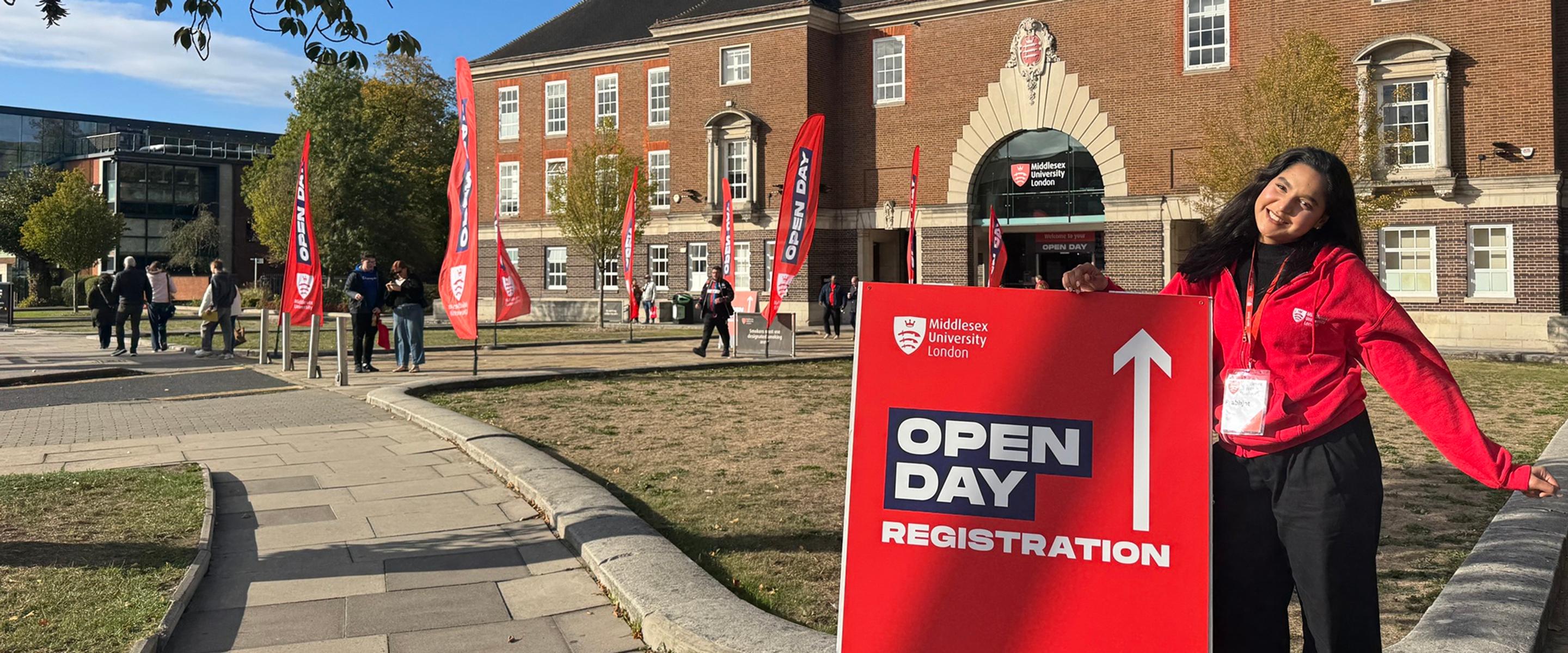 A student next to a sign for open day registration, outside the College Building of Middlesex University London