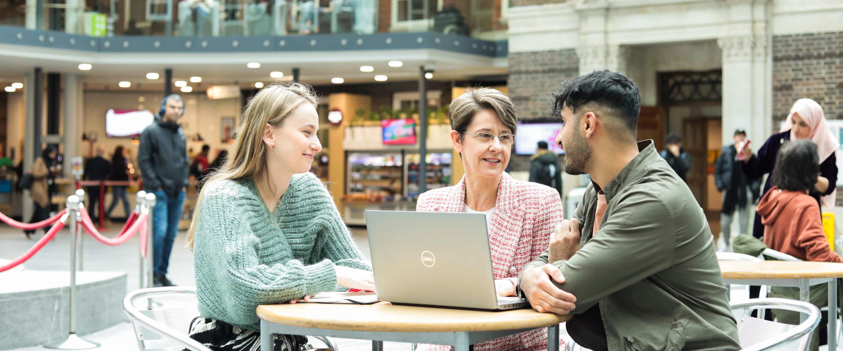 Staff sitting in the Quad building looking at a laptop and talking
