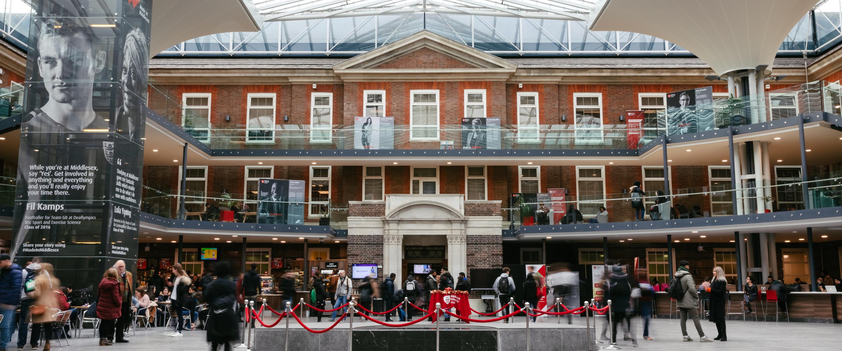a wide view of the atrium in the quad at middlesex university showing three floors and students standing, sitting and walking about
