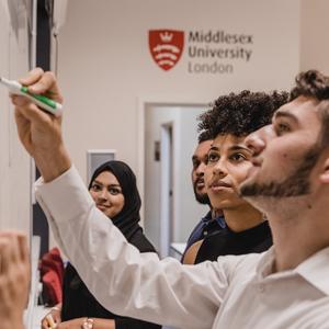 A group of students in discussion and writing on a whiteboard in a classroom