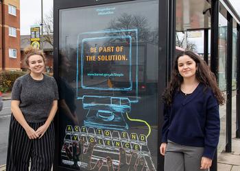 Two students stand either side of a bus stop showing their campaign poster