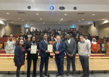 A line-up of Computer Science lecturers and staff stand with two Nigerian visitors to Middlesex in a lecture theatre in Hatchcroft building