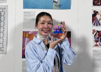 Middlesex University graduate Lotte Siu holds her award in front of a display of illustration