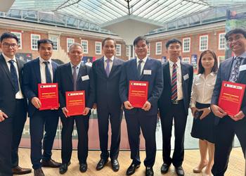 A line-up of visitors to MDX from University of Oxford and Vietnam, four of them holding red certificates representing an MOU between MDX and their institutions
