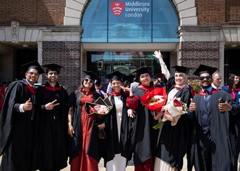 A group of enrobed graduates celebrating in front of the main Middlesex University London entrance