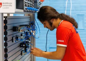 A student with a ponytail and sideburns works intently on an electronic circuit