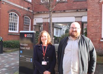 Two people stand next to a university sign