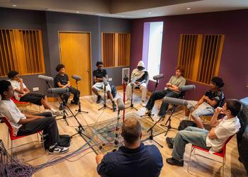 Group of young boys sitting in a circle and recording a podcast in a studio.