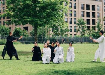 A group of dancers in black and white costumes flowing costumes strike dramatic poses in Colindale Park