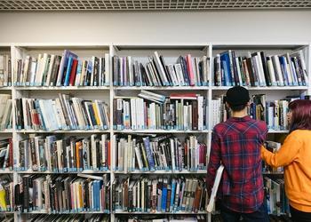 Two students look at books in a library