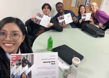 Students hold up certificates at a desk