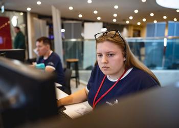 A young woman in a WorldSkills top and a lanyard sits at a computer as she takes part in a Digital Construction skills competition