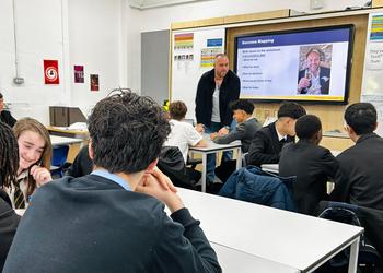 Male school pupils in a classroom watching an adult male standing up at a whiteboard