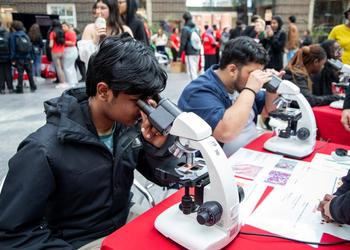 Two young men looking through microscopes at a science festival