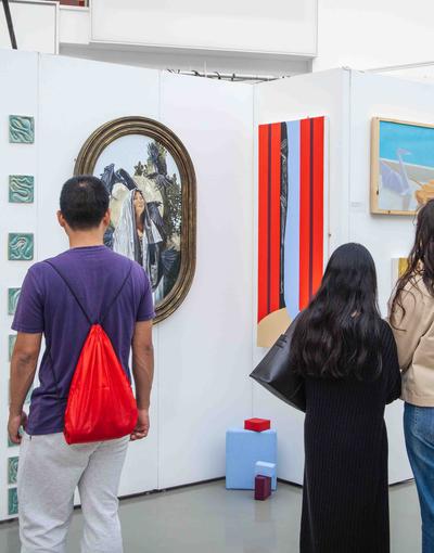 Three people look at artwork in a gallery