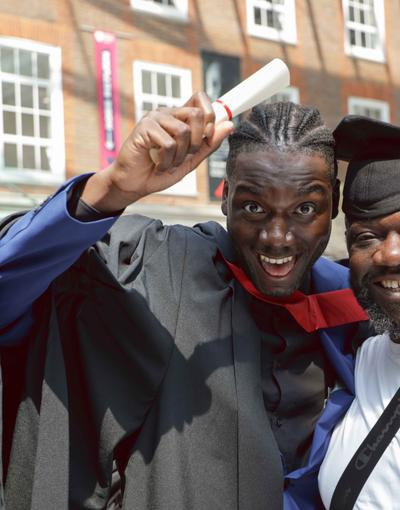 Graduating student with a friend or relative, holding their graduation scroll and looking happy