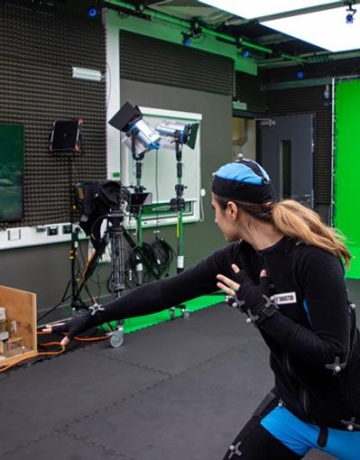 A person in a motion capture suit pushing their fist forward, with an animated soldier on a screen emulating the action
