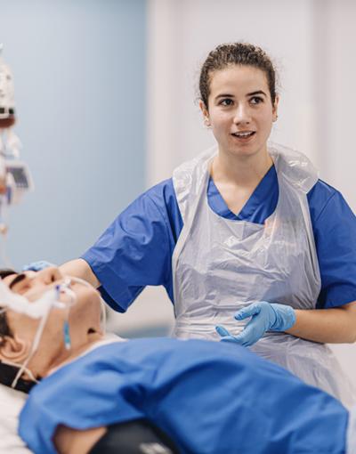 A nursing student attends to a dummy patient in a medical simulation suite