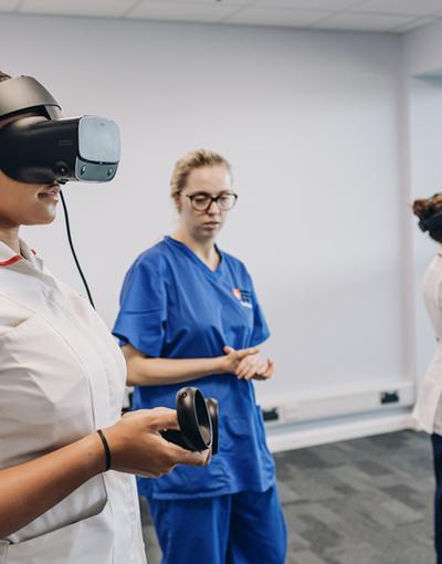 Nursing students using VR headsets under supervision of a woman wearing nursing scrubs