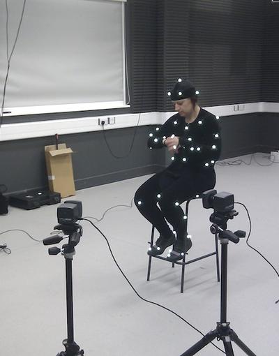 A student sitting on a stool wearing a motion capture suit. There are several cameras pointing at her