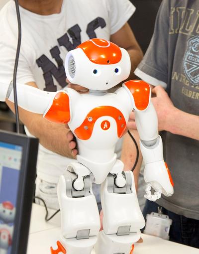 Two student holding a small white and orange robot, lifting its right arm