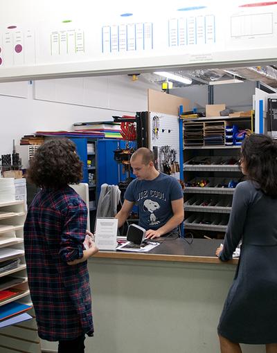 Three students in a store with one behind a counter serving the other two