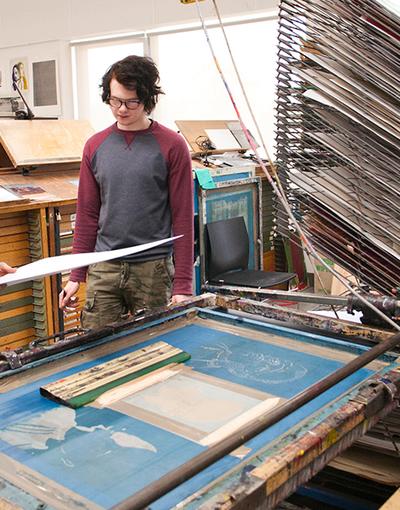 A student holding a piece of paper over a giant printing machine