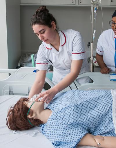 student midwife works with a pregnant dummy while teacher watches on