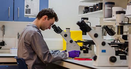 A scientist in a lab coat examines a microscope, focusing on the tiny details of a specimen.