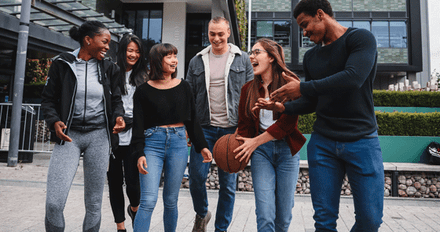 A diverse group of young adults walking together in a park, chatting and laughing, enjoying each other's company.