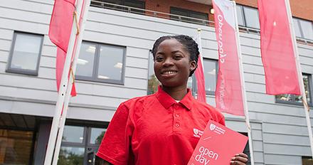A woman in a red shirt holding a book at an open day event.