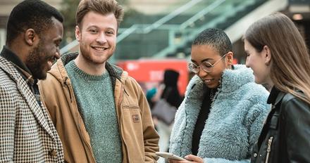 Three young people excitedly looking at a cell phone screen, engrossed in a virtual-experience.
