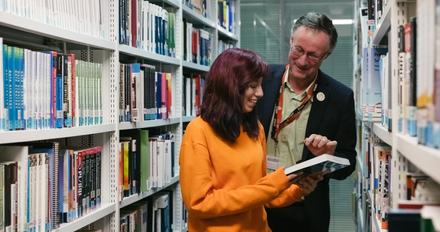 A man and woman in a library, engrossed in books.