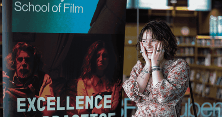 A student standing in front of a banner School of Film