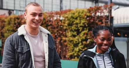 Two young people happily walking side by side, wearing casual clothes and smiling at each other.