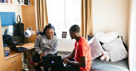 two students sit in bedroom studying together