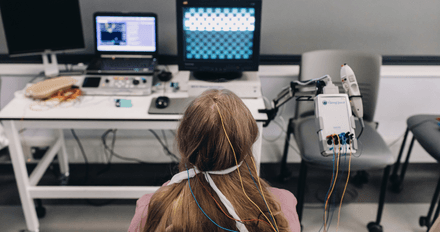 A woman sits at a computer with a robotic arm in a healthcare-science lab, demonstrating the integration of technology in medical research.